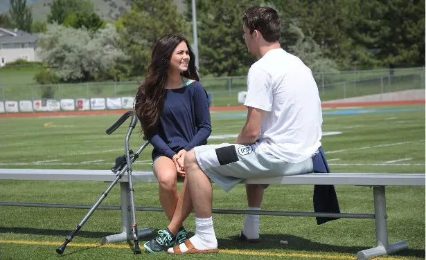 Teenagers talking on bench with crutch at sports field.