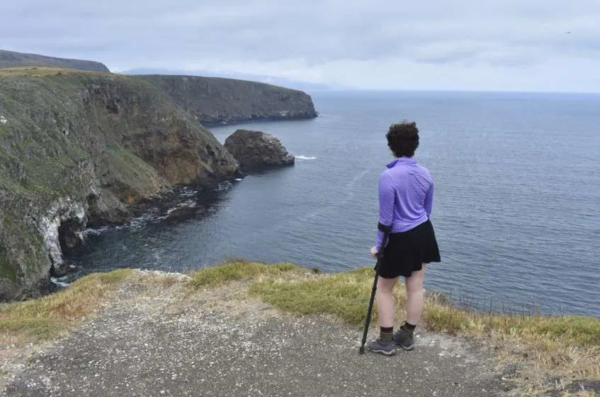 Person with in-Motion crutches overlooks ocean cliff view.