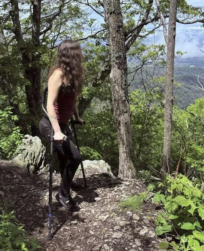 Woman hiking with crutches on forest trail.