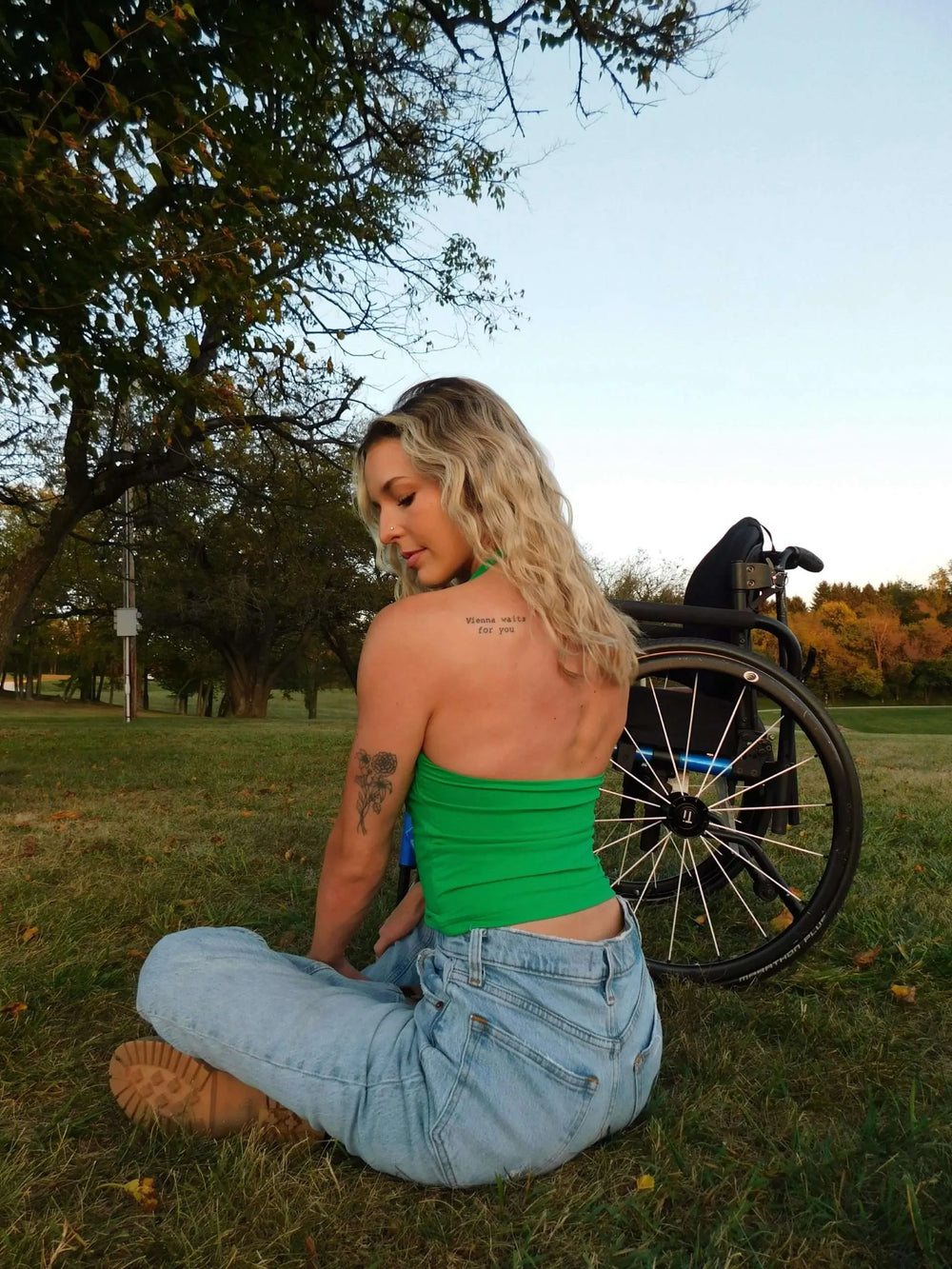 Woman sitting by wheelchair in park setting.