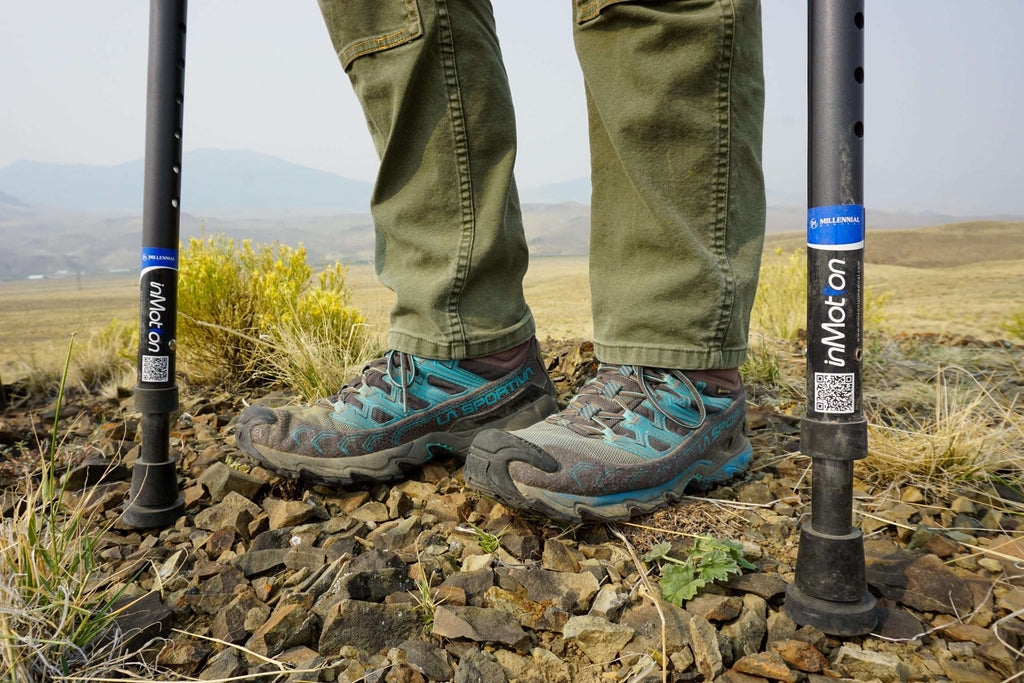 Person hiking on rocky terrain with trekking poles.