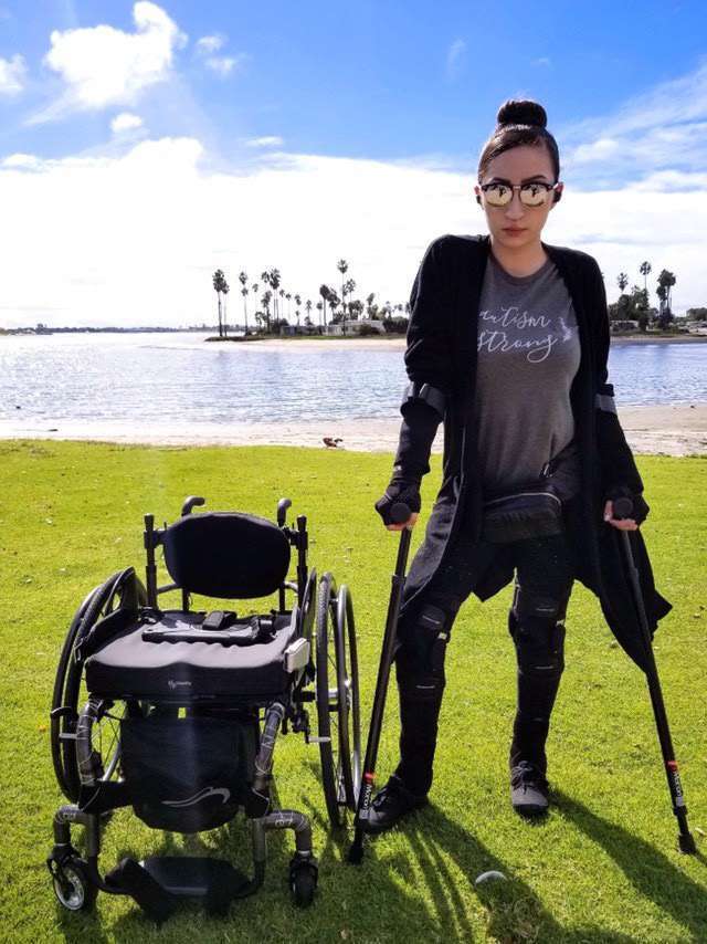 Person with crutches beside wheelchair by a lake.