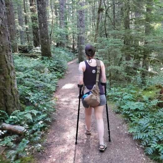 Person hiking with crutches in forest trail.