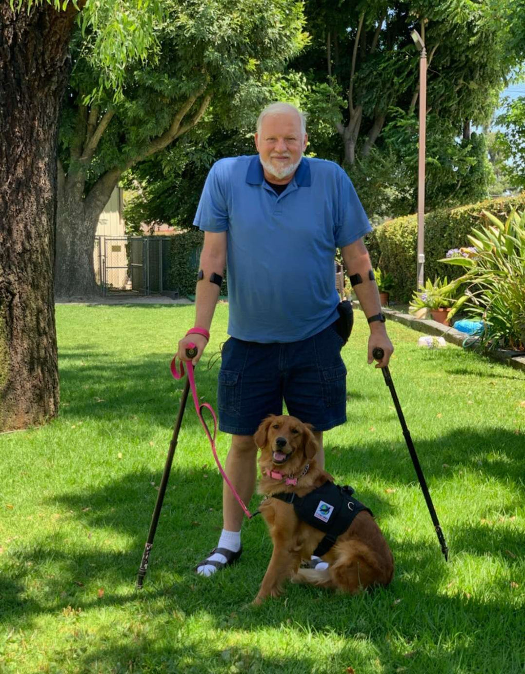 Man with crutches and service dog in garden.